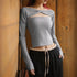 Person wearing a gray long-sleeve crop top with cut-out design and black pants against a wooden wall.